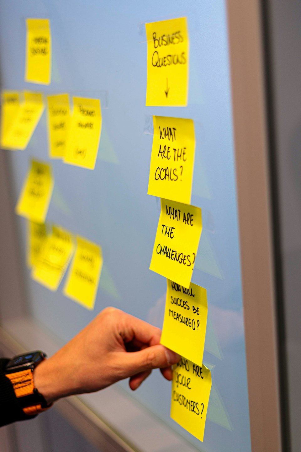 A hand places yellow sticky notes on a glass board.